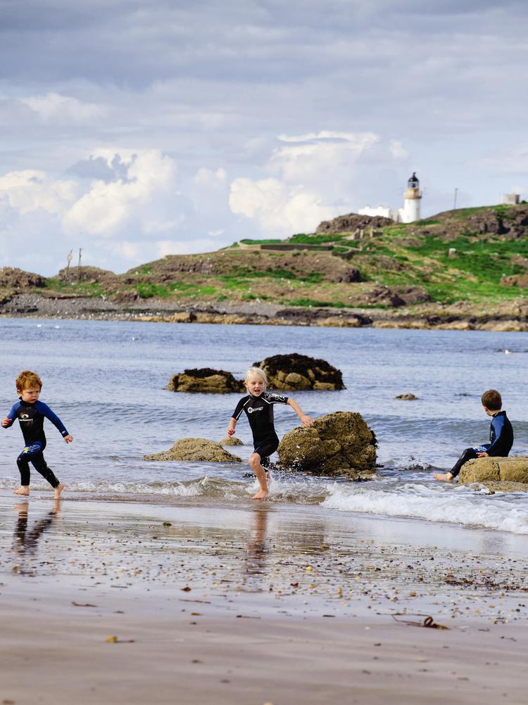 Dzieci w piankach surfingowych biegaja po plaży Yellowcraigs
