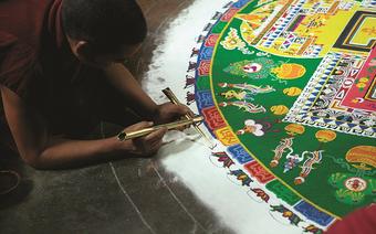 Przygotowanie mandali – mnich sypie piasek o różnych kolorach, ziarnko po ziarnku