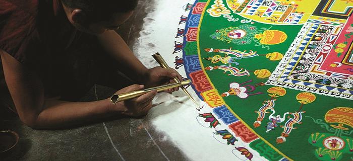Przygotowanie mandali – mnich sypie piasek o różnych kolorach, ziarnko po ziarnku